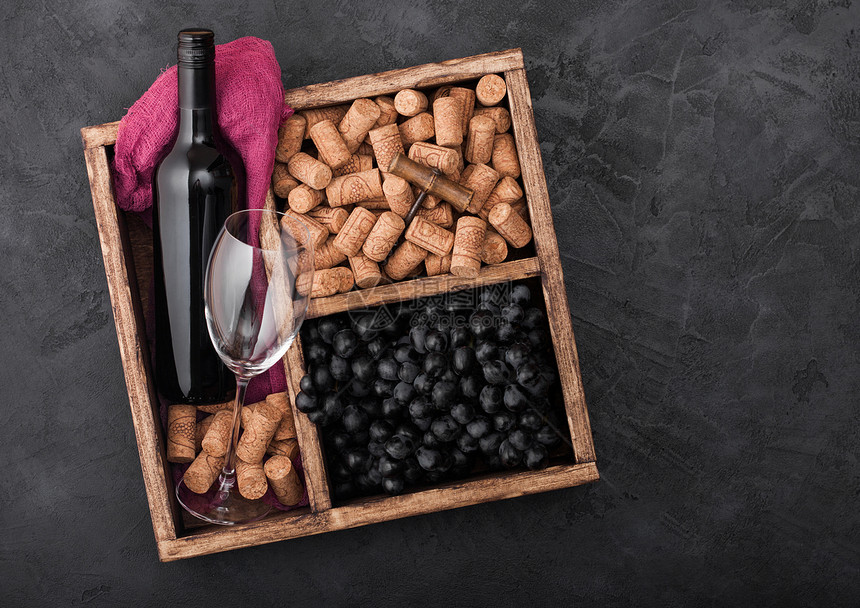 白葡萄和深的空玻璃瓶装红葡萄酒和空杯子装有软木箱和装在黑色石头背景和红布的旧木箱内图片