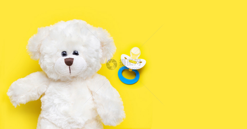 黄色背景上的玩具白熊和婴儿奶嘴图片