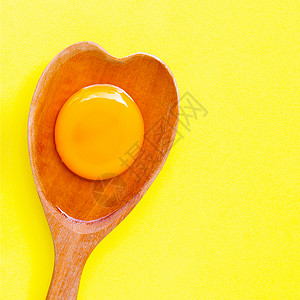黄色背景的木勺心形上蛋和白高清图片