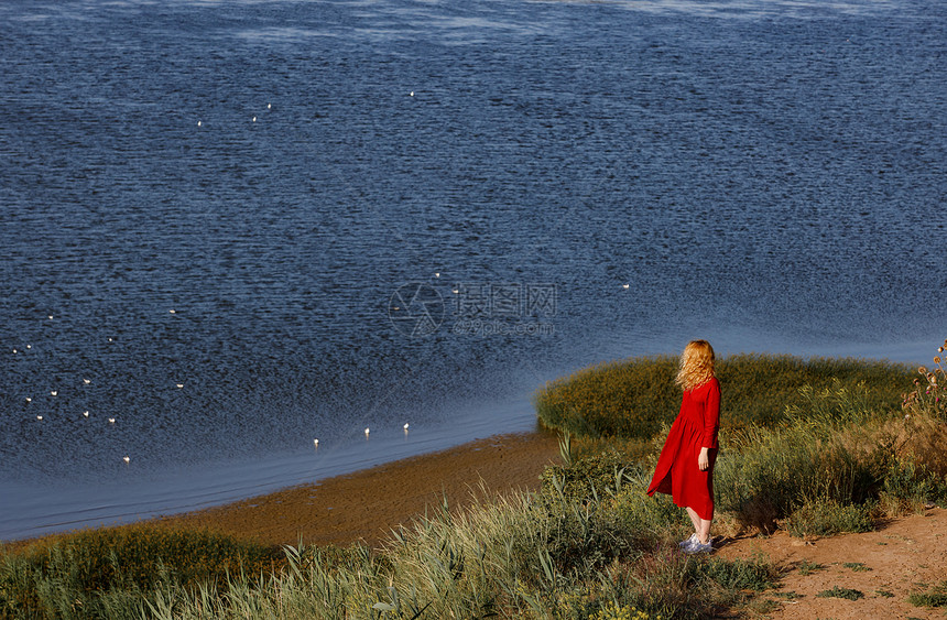 穿着红裙子的女人在日出时沿着海岸行走图片