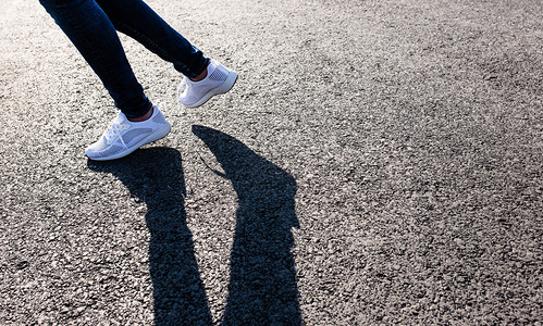 穿着白色运动鞋的女子在日落时沥青路上向日落时晒在沥青路向日晒在沥青路向日晒背景图片
