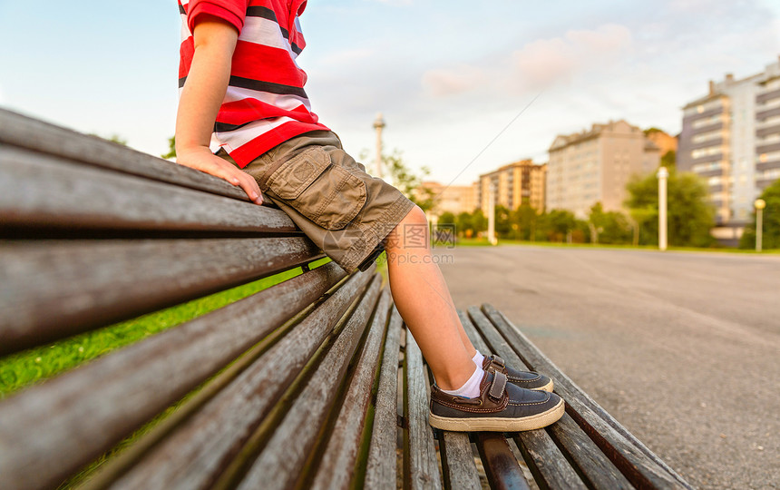 在无聊的夏日里穿着短裤坐在木凳公园顶上放松的男孩腿特写镜头男孩双腿坐在公园长凳上放松图片
