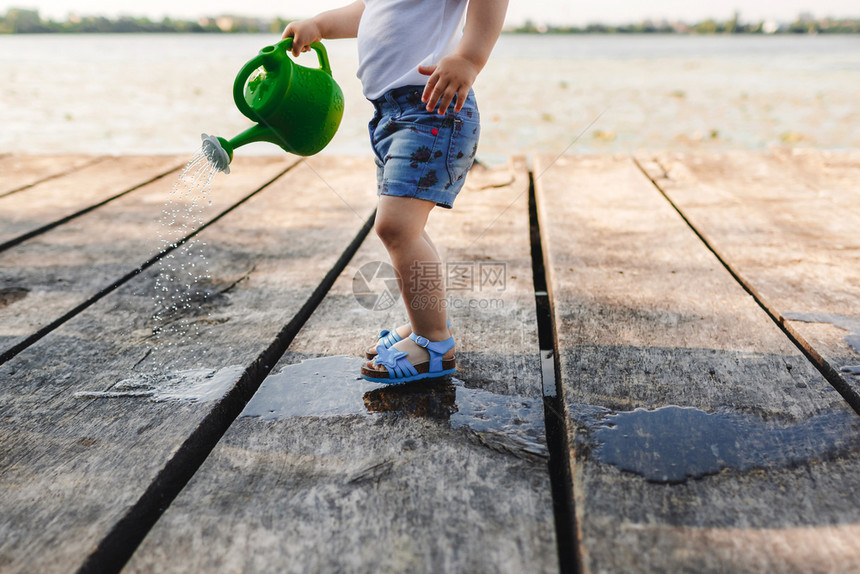 一个小女孩在玩木桥的水罐春天和夏园艺绿色水罐图片