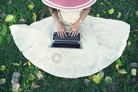 使用笔记本电脑在绿色玻璃园子上拍摄的年轻妇女顶部照片商业和技术概念图片