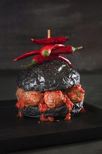 黑面包汉堡有肉丸和辣番茄酱在黑盘和桌子上浅的奇异汉堡形象怪的食物圣餐背景图片