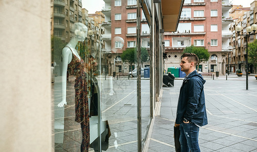 年轻男子拿着购物袋看商店的窗户购买礼品男子看着商店的窗户购买礼品图片