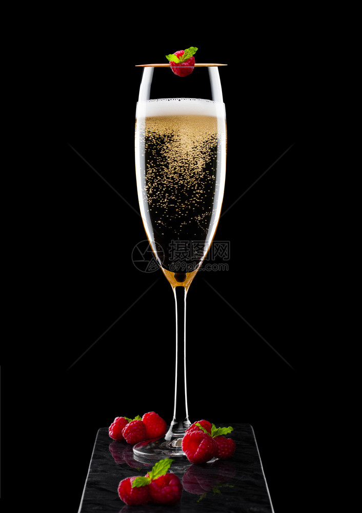 高雅的黄色香槟杯子上面有彩虹和新鲜的浆果还有黑大理石板上粘着薄荷叶的图片