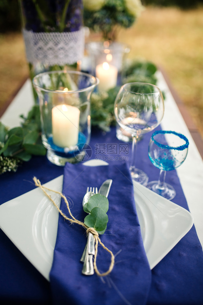 在树林的木制板上有花朵安排蓝色白绿花朵和蜡烛雕塑玻璃餐具照片贴近装饰细节在树林的木制板上有蓝色绿花朵和餐具图片