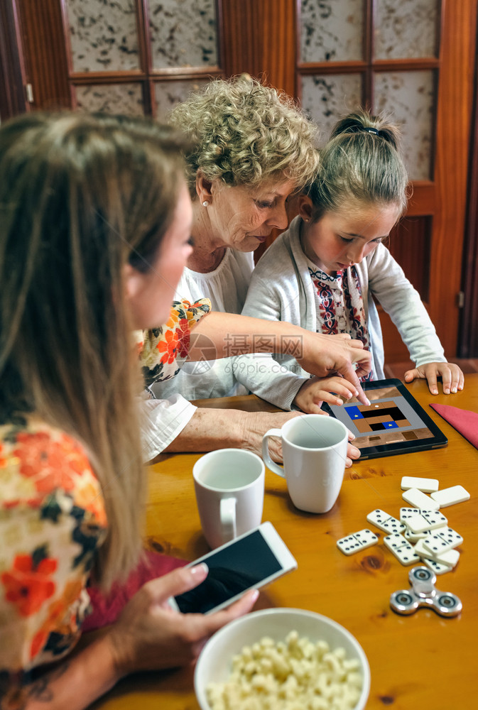 外祖母和孙女在平板上玩游戏而母亲则在平板上看外祖母和孙女在平板上玩游戏图片