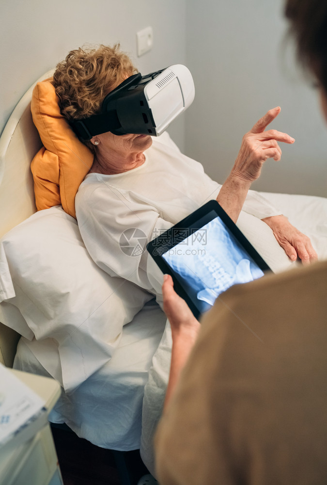更年长的病人使用虚拟现实眼镜去看脊椎而女医生解释图片