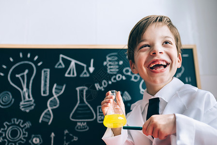 帕格标记快乐的小科学家在用标记瓶中显示黄色液体时笑的肖像快乐Kig笑和在瓶中显示液体背景
