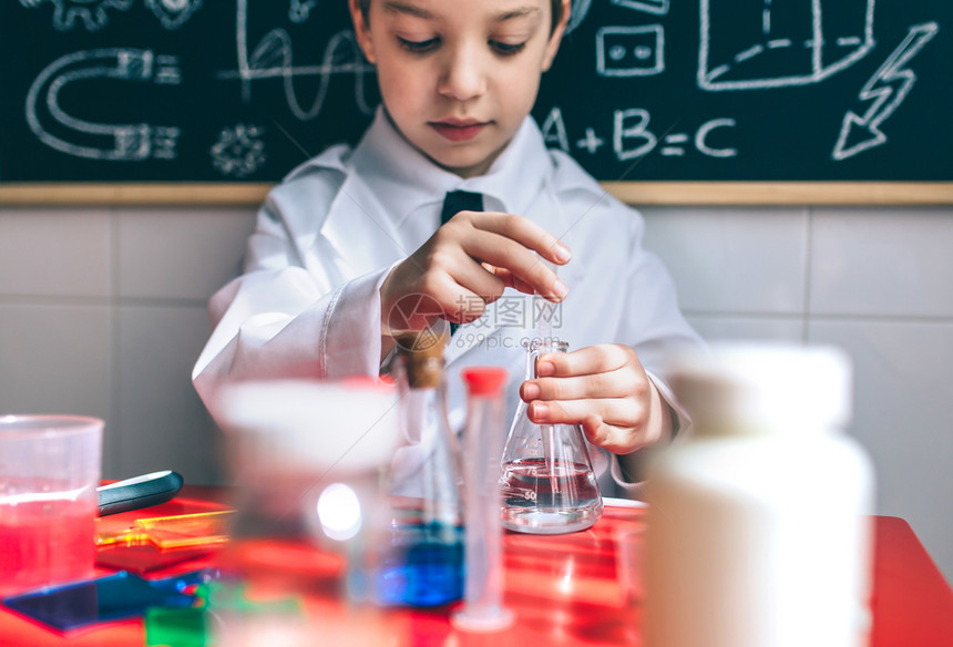 小男孩科学家的肖像从瓶子上提取液体与粉笔板对面画选择地聚焦于瓶子上严重玩化学液体的小孩图片