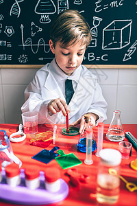 小男孩科学家肖像将多彩化学液体混在一起与粉笔板和绘画相对图片