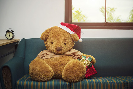 大熊有圣诞帽子和红礼盒在沙发上圣诞快乐的背景概念高清图片