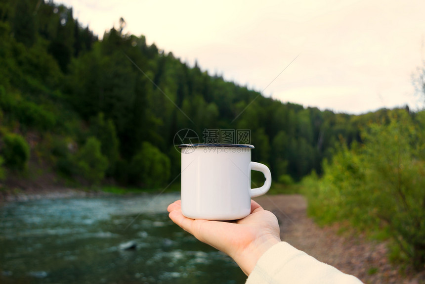 女人拿着白色的营火罐头杯装有河边风景空的杯子装上设计宣传品图片