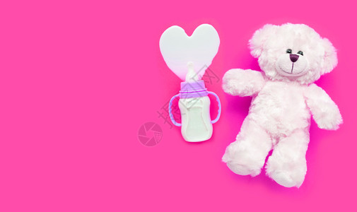 粉红色背景上带有玩具白熊的婴儿奶瓶复制空间图片