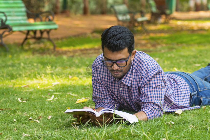 年轻男性在公园草地上读书图片
