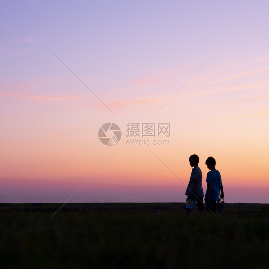 两名男孩的休眠带着桶子防止多彩的日落图片