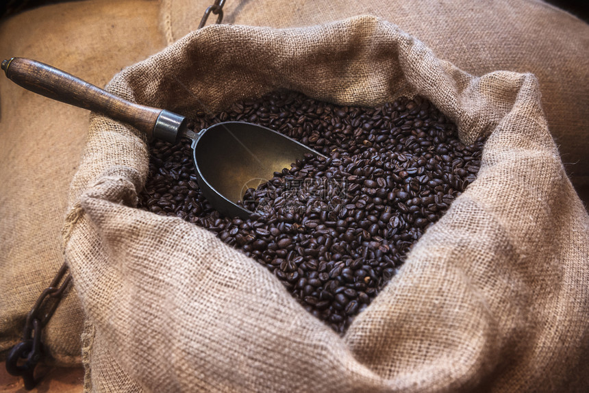 在黄麻袋中烤黑咖啡豆和一把旧勺子黄麻包装中咖啡豆的古老形象用咖啡豆打开黄麻袋图片