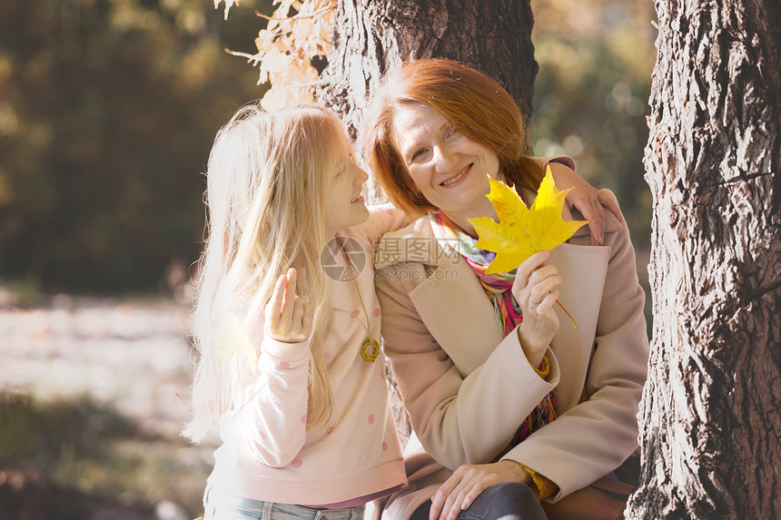 母亲和女儿在公园中手持黄色的红树叶图片