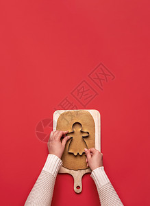 最小姜饼人女手切姜饼孩从干面团在一个木制切板和红色背景家里烘烤圣诞节甜点以上观看xmas食品背景