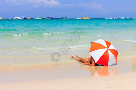 在沙滩上用橙色的雨伞做妇女日光浴图片