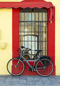 灰色自行车在黄外墙和红窗口前自行车和后备箱图片