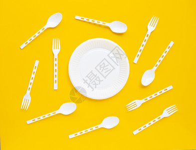 黄色背景上的塑料盘子勺和叉图片