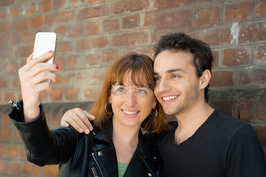 快乐的年轻夫妇在城里玩自拍手机有趣的概念图片