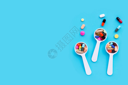 白勺子配有丰富多彩的药丸片和胶囊蓝底背景复制空格图片