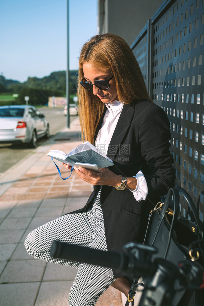 商业女人在街头阅读日记与她的摩托车下一站商业女人在阅读日记与她的摩托车下一站图片