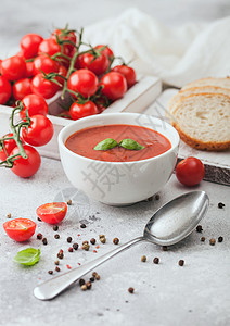 加兹帕乔白碗盘的奶油番茄汤匙在浅底背景上一盒生西红柿和面包背景
