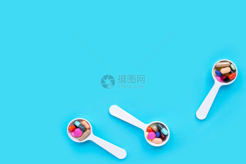 白勺子配有丰富多彩的药丸片和胶囊蓝底背景复制空格图片