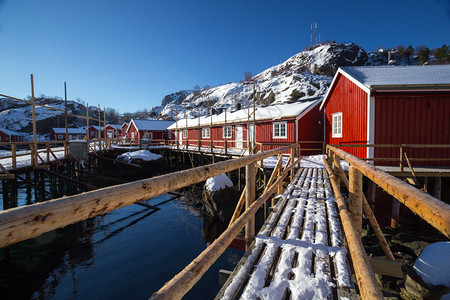 传统的挪威木制屋站在峡湾的岸边和远处山上岛屿北部高清图片