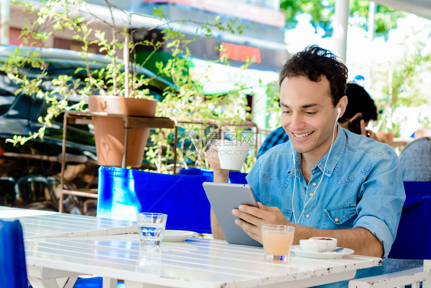 有耳机的拉丁年轻人在咖啡店里用数字平板电脑图片