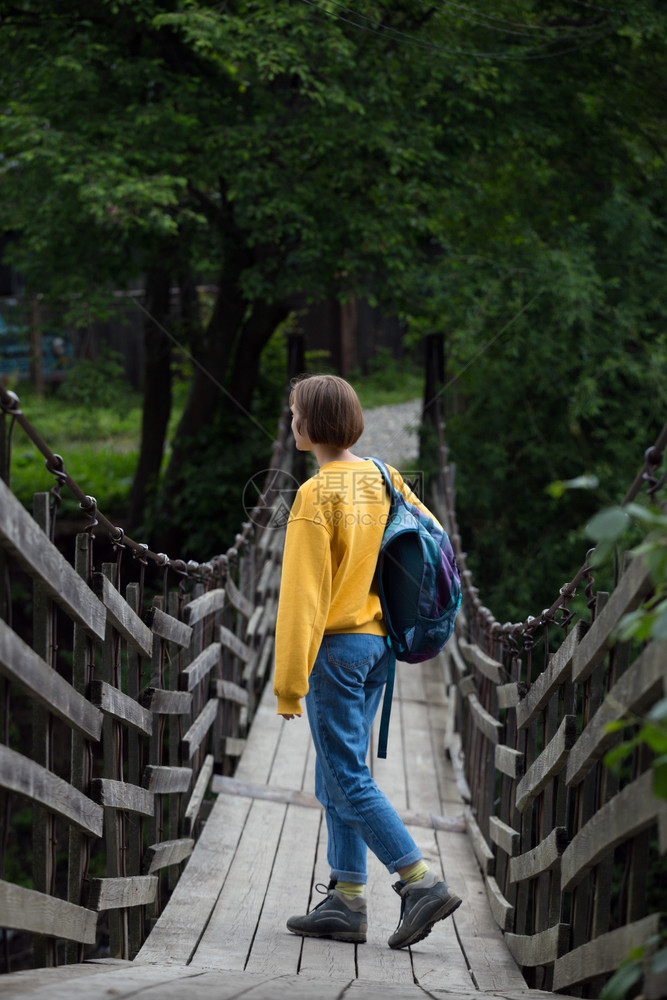 女孩徒步旅行者背包站在悬吊桥上图片