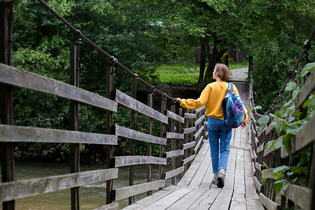 女孩徒步旅行者背包站在悬吊桥上图片