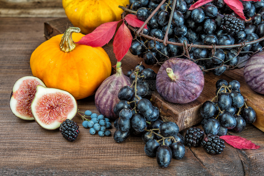 篮子中的黑葡萄和成熟无花果红草莓橙色南瓜和木本底有秋叶的黑莓图片