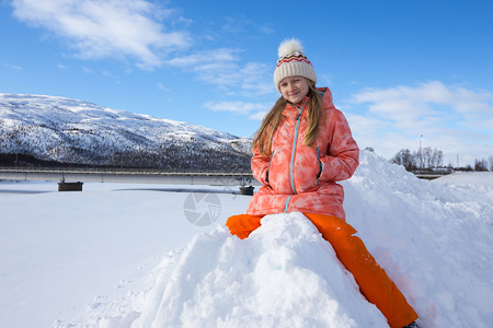 可爱的小女孩坐在雪堆上玩耍图片