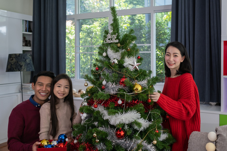 亚足幸福的家庭父亲母女儿帮助准备和赠送或装饰在客厅的圣诞树或装饰图片