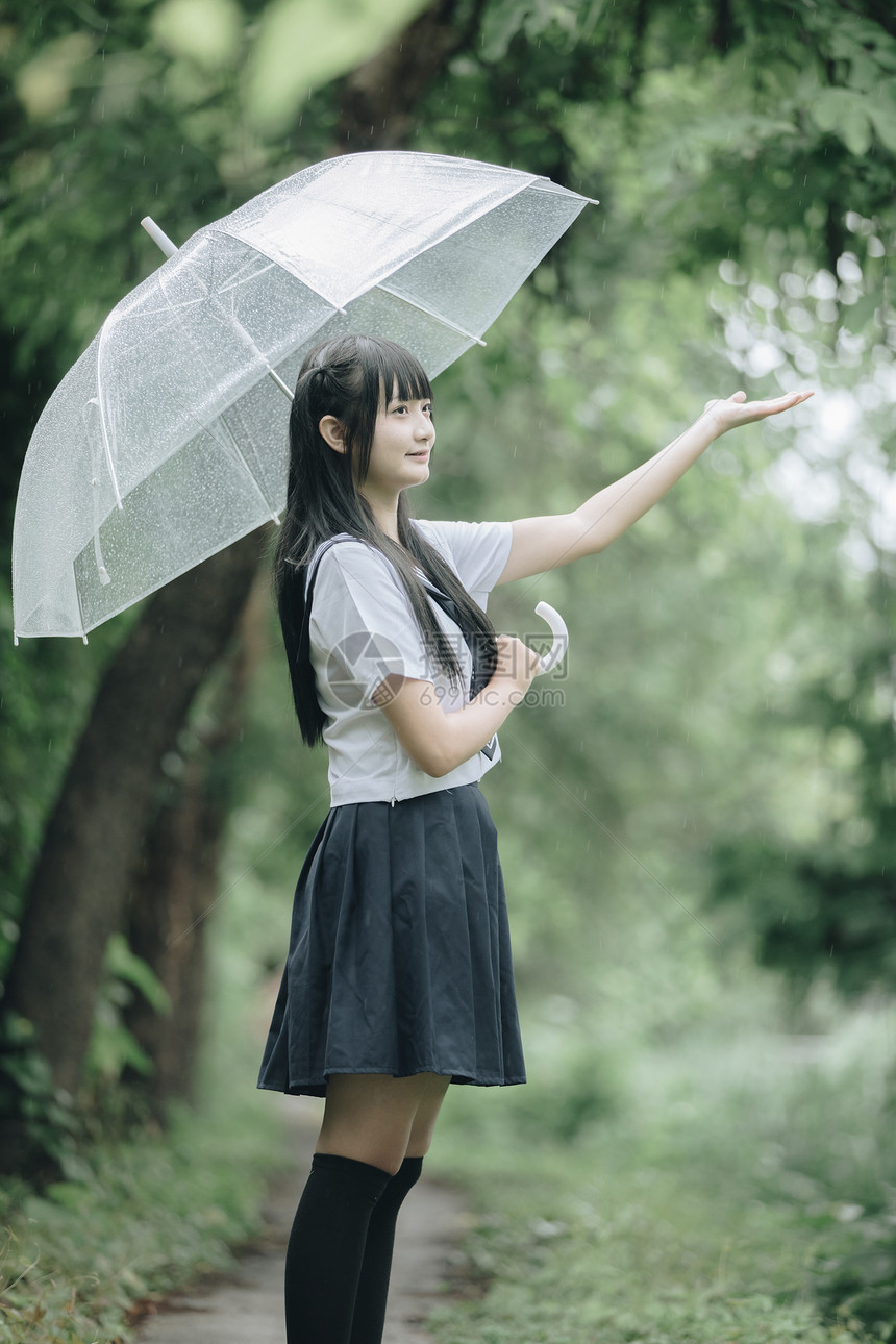 下雨时在自然行走道上带着雨伞行走的亚裔女学生肖像图片