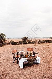 野外餐非洲风格的木制导演椅子桌上摆着酒桶SanegtiSanv森林的非洲户外餐厅背景图片