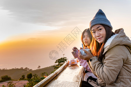 两个亚洲女人坐在山顶的日出喝咖啡图片