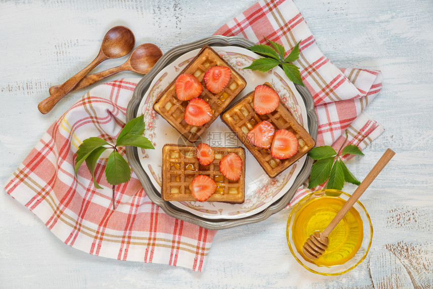 鲜草莓和蜂蜜的甜华夫饼放在一个美丽的盘子上站在一块压碎的餐巾纸上图片