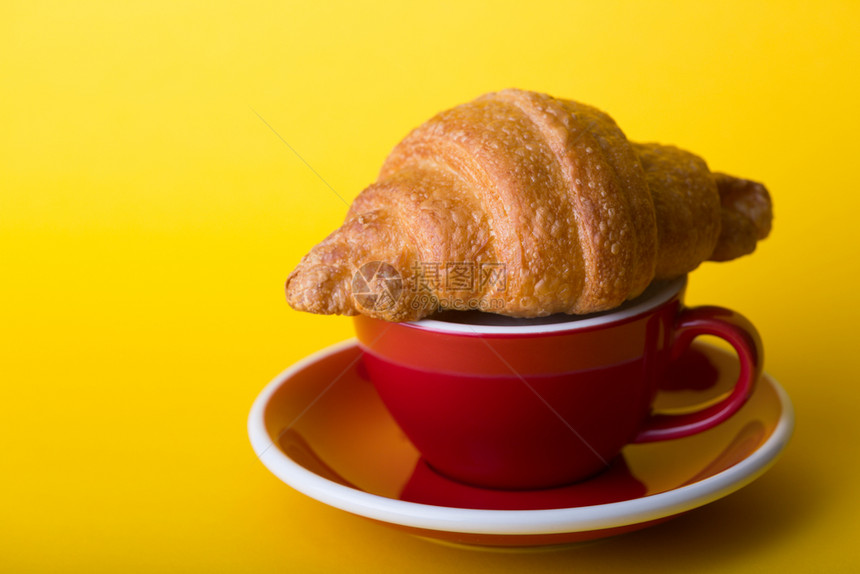 黄底带卡布奇诺和羊角面包的美丽咖啡红杯图片