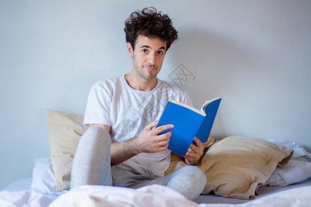 年轻拉丁男人躺在家里睡觉时读一本书图片