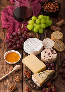 玻璃红葡萄酒在板上挑选各种奶酪和木制桌底的葡萄蓝色stilon红色的李斯特脆奶酪和蜂蜜背景