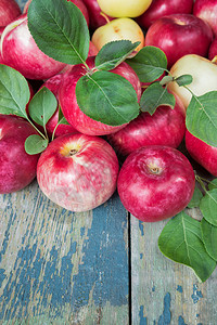许多红苹果绿色叶子在旧木制桌上图片