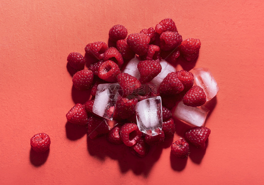 在阳光下红底的冰块堆放着新鲜的草莓上面是美味的夏季水果浆柠檬的原料图片