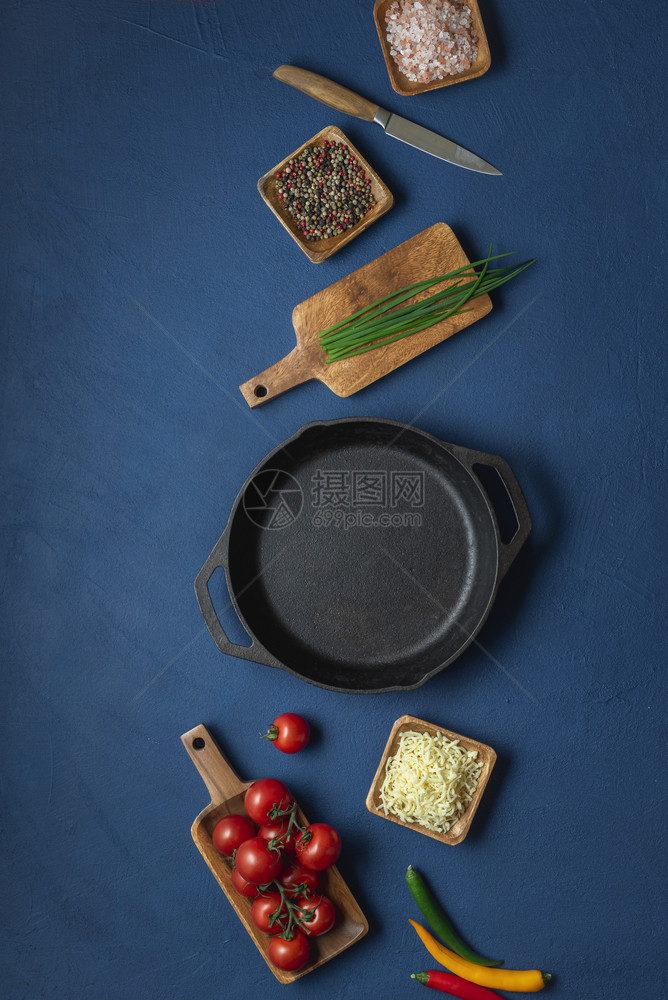 黑锅和食物成分奶酪西红柿和洋葱放在蓝色桌子上图片